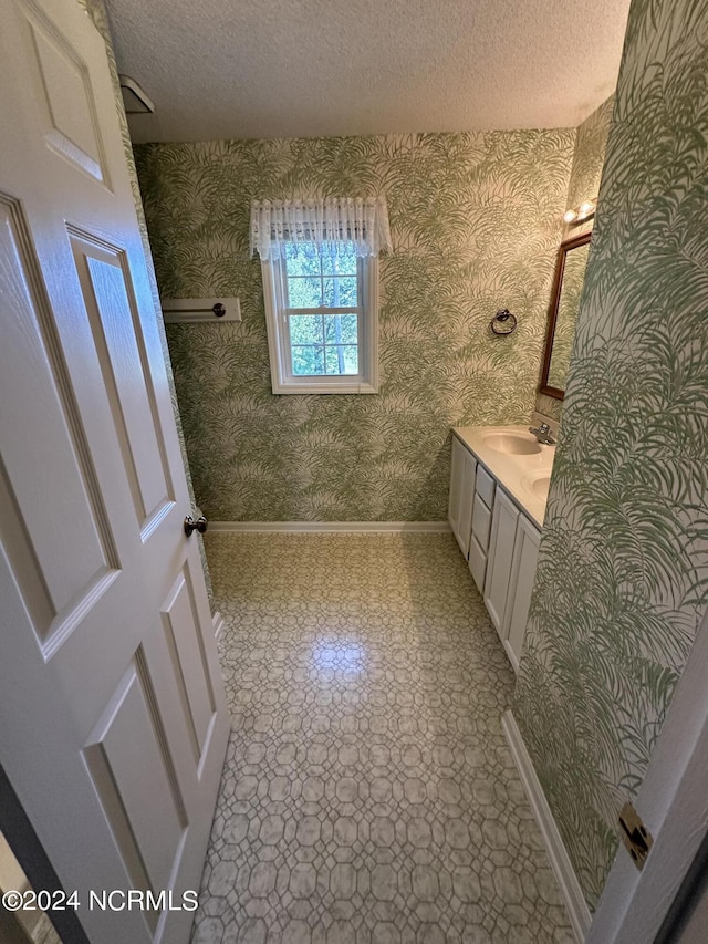 bathroom with baseboards, a textured ceiling, vanity, and wallpapered walls