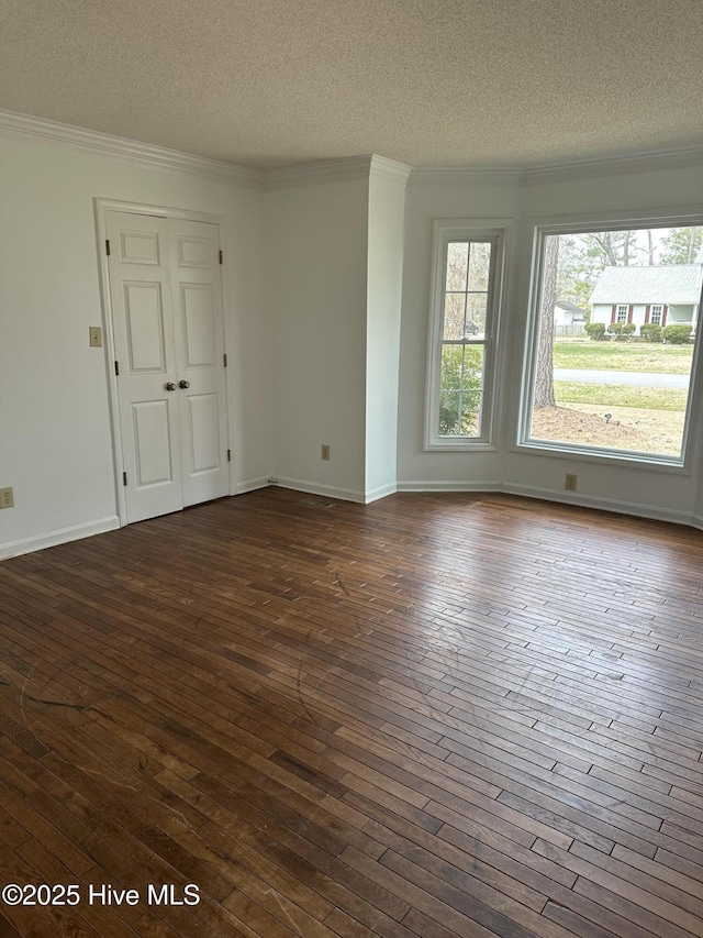 spare room with a textured ceiling, dark wood-style flooring, baseboards, and crown molding