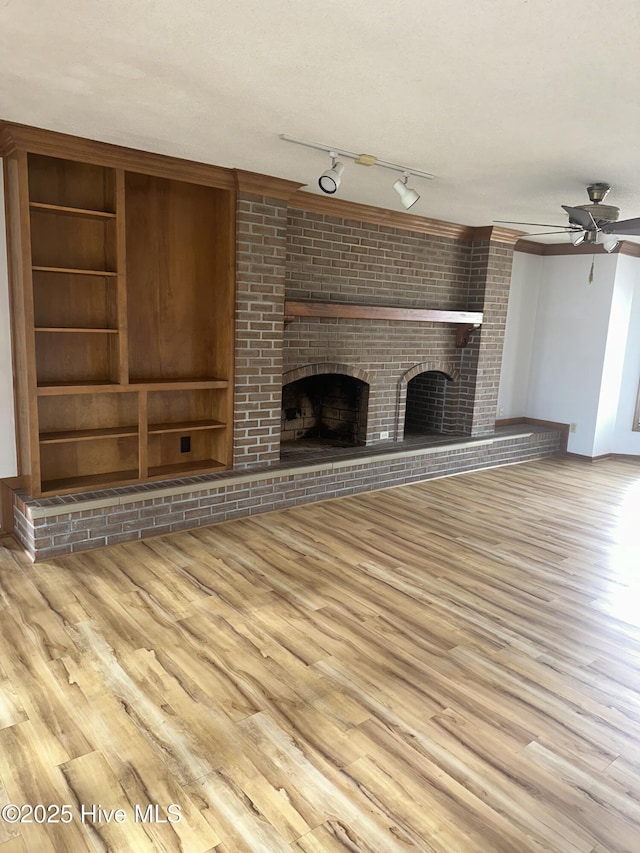 unfurnished living room with a brick fireplace, ceiling fan, built in features, and wood finished floors