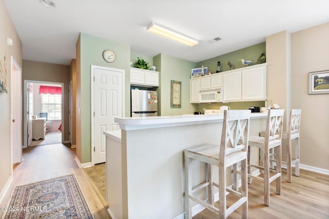 kitchen with light hardwood / wood-style flooring, white cabinetry, kitchen peninsula, and stainless steel refrigerator