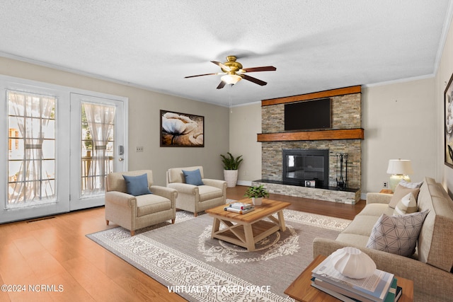 living room featuring a textured ceiling, wood-type flooring, a stone fireplace, and ceiling fan