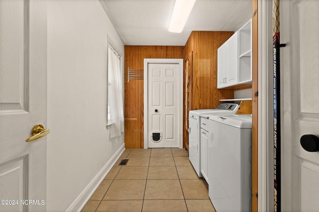 washroom with cabinets, a textured ceiling, light tile patterned flooring, wooden walls, and independent washer and dryer