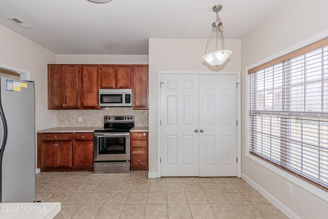 kitchen with light tile patterned floors, appliances with stainless steel finishes, decorative light fixtures, and decorative backsplash