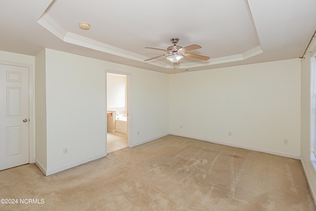 unfurnished bedroom with connected bathroom, light carpet, a tray ceiling, and ceiling fan