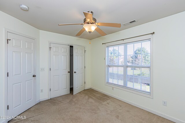 unfurnished bedroom featuring light carpet, multiple windows, and ceiling fan