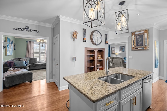 kitchen featuring light stone counters, sink, pendant lighting, dishwasher, and an island with sink