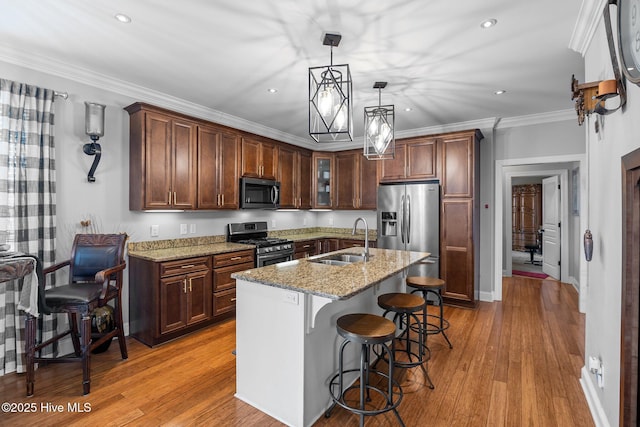 kitchen with appliances with stainless steel finishes, a kitchen breakfast bar, light stone counters, sink, and a center island with sink