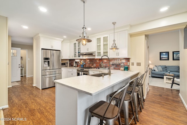 kitchen featuring a breakfast bar area, decorative light fixtures, appliances with stainless steel finishes, hardwood / wood-style flooring, and white cabinets