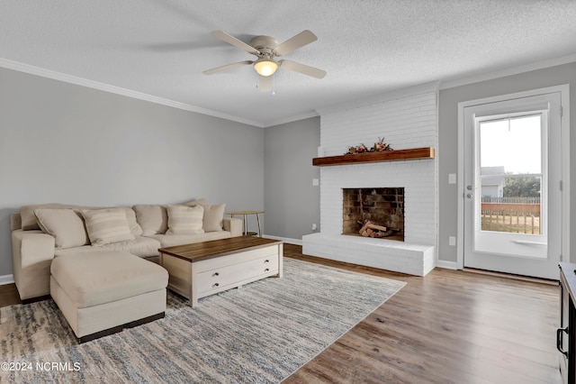 living room featuring ceiling fan, ornamental molding, wood-type flooring, a textured ceiling, and a fireplace