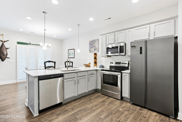 kitchen featuring sink, kitchen peninsula, decorative light fixtures, stainless steel appliances, and dark hardwood / wood-style flooring