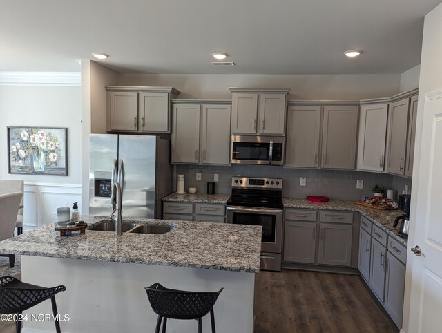 kitchen with gray cabinetry, stainless steel appliances, dark hardwood / wood-style flooring, a breakfast bar area, and decorative backsplash