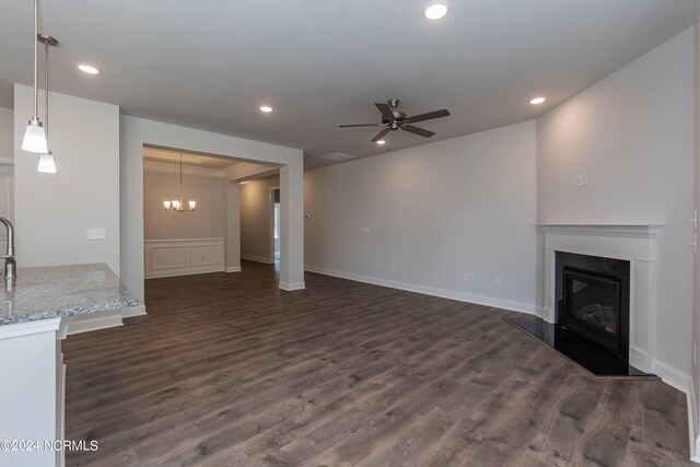 unfurnished living room with ceiling fan with notable chandelier and dark wood-type flooring