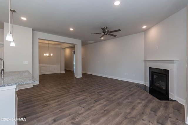 unfurnished living room with ceiling fan with notable chandelier and dark wood-type flooring