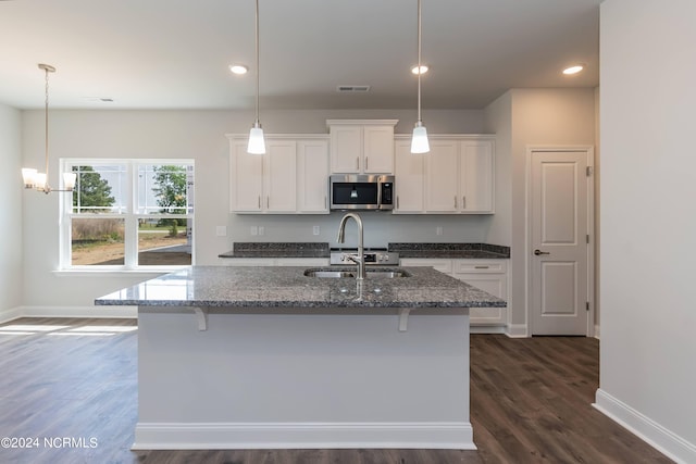 kitchen with dark hardwood / wood-style flooring, white cabinetry, an island with sink, and dark stone counters