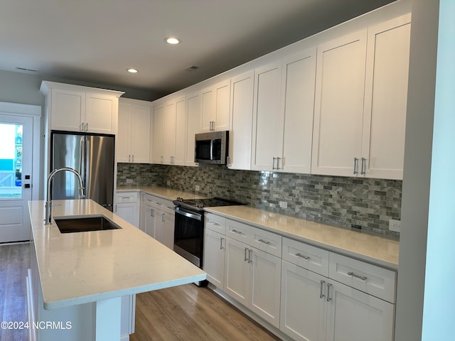 kitchen featuring appliances with stainless steel finishes, an island with sink, sink, light wood-type flooring, and white cabinets