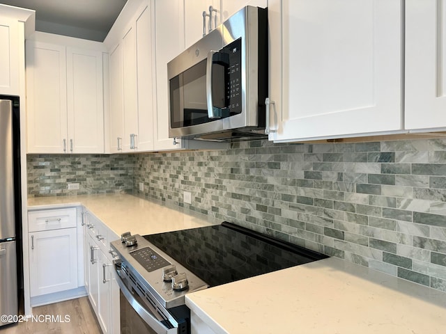 kitchen featuring light wood-type flooring, tasteful backsplash, light stone countertops, appliances with stainless steel finishes, and white cabinets