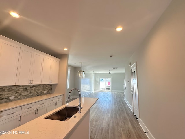 kitchen with hardwood / wood-style flooring, light stone counters, white cabinetry, sink, and pendant lighting