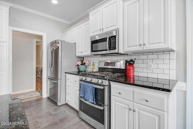 kitchen featuring appliances with stainless steel finishes, dark stone counters, white cabinets, and crown molding