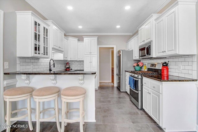 kitchen with appliances with stainless steel finishes, glass insert cabinets, white cabinetry, dark stone counters, and a peninsula