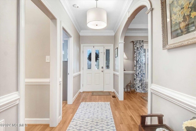 entrance foyer with ornamental molding, arched walkways, baseboards, and light wood finished floors