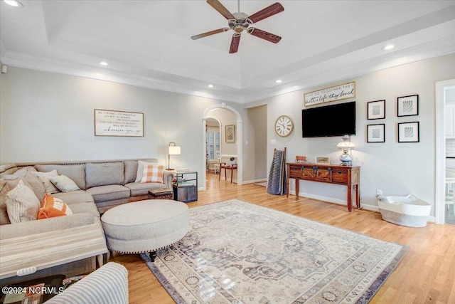 living room featuring arched walkways, a raised ceiling, and wood finished floors