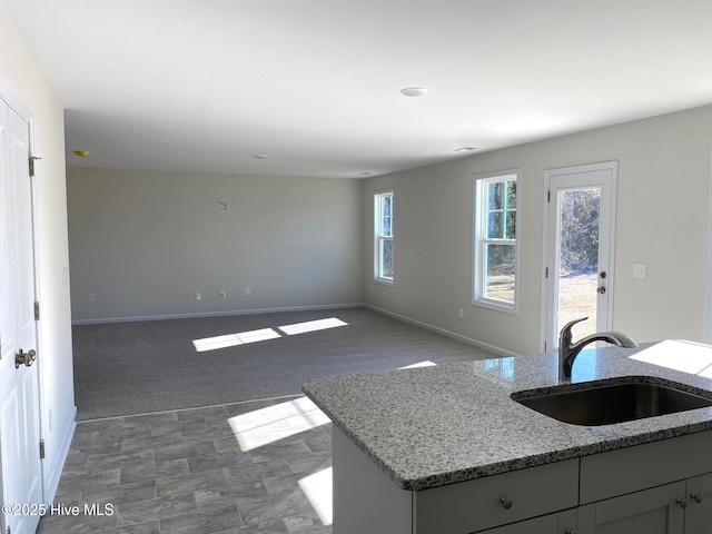 kitchen featuring a center island with sink, sink, gray cabinetry, light stone counters, and dark colored carpet