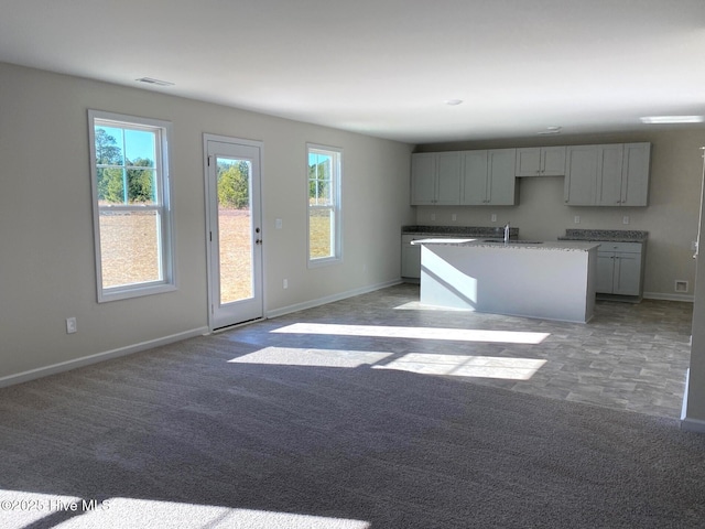 kitchen with light carpet, gray cabinets, sink, and a kitchen island with sink