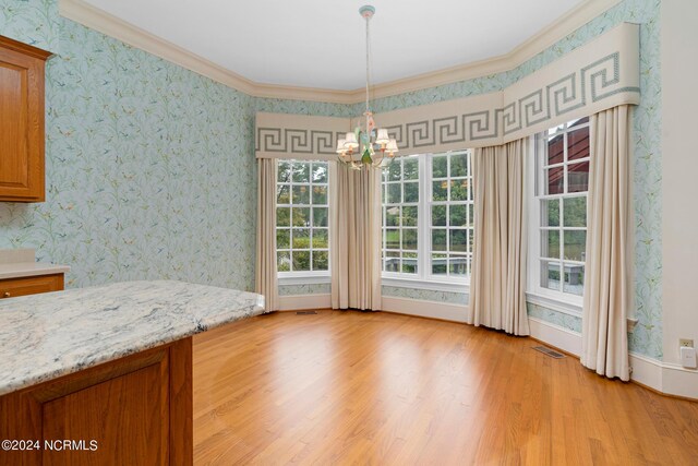 unfurnished dining area with an inviting chandelier, ornamental molding, and light hardwood / wood-style floors