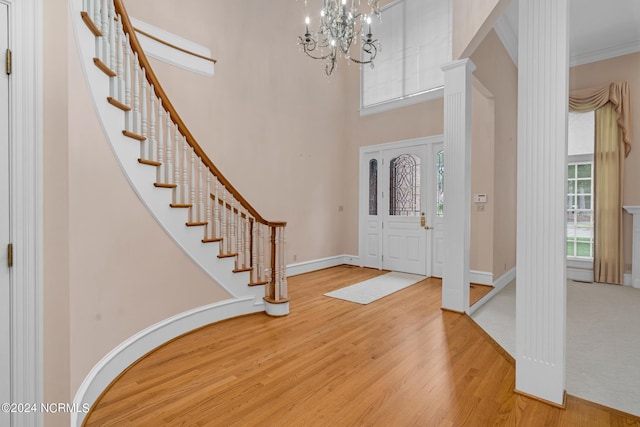 entryway with crown molding, a towering ceiling, wood-type flooring, and a chandelier