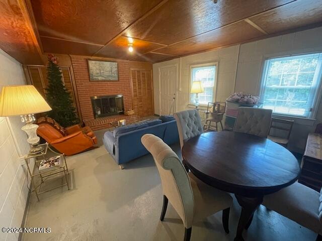 dining room featuring wood ceiling, a brick fireplace, and concrete flooring