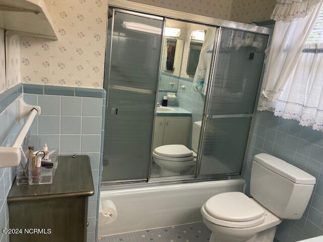 612 David St, Elizabethtown, NC 28337 - full bathroom with wallpapered walls, tile walls, toilet, a wainscoted wall, and bath / shower combo with glass door
