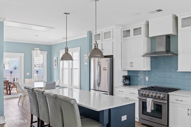 kitchen featuring a kitchen island, hardwood / wood-style flooring, wall chimney exhaust hood, hanging light fixtures, and stainless steel appliances