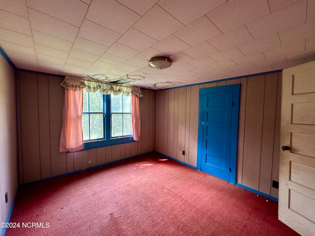 carpeted spare room featuring wood walls