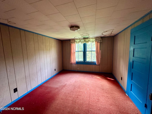 carpeted empty room featuring wood walls