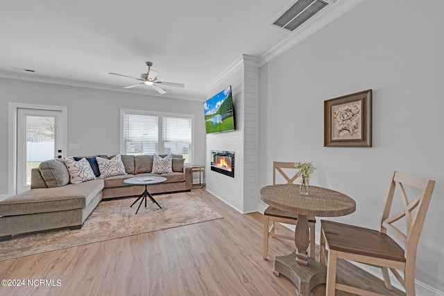 living room with ornamental molding, light wood-type flooring, ceiling fan, and a large fireplace