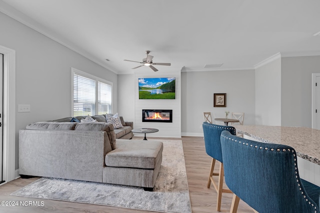 living room featuring ceiling fan, ornamental molding, and light wood-type flooring