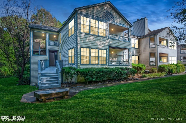 back house at dusk featuring a balcony and a lawn