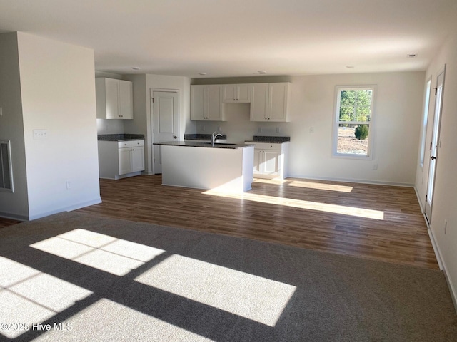 kitchen with dark wood-type flooring, white cabinetry, sink, and an island with sink