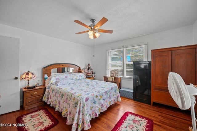 bedroom with a textured ceiling, ceiling fan, and dark hardwood / wood-style flooring