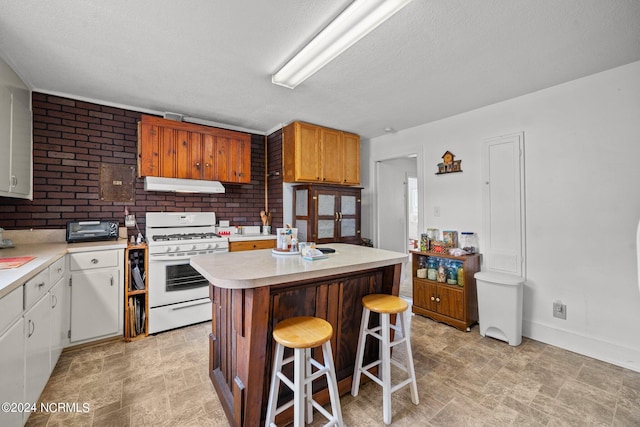 kitchen with white range with gas cooktop, a textured ceiling, a center island, a breakfast bar area, and white cabinets