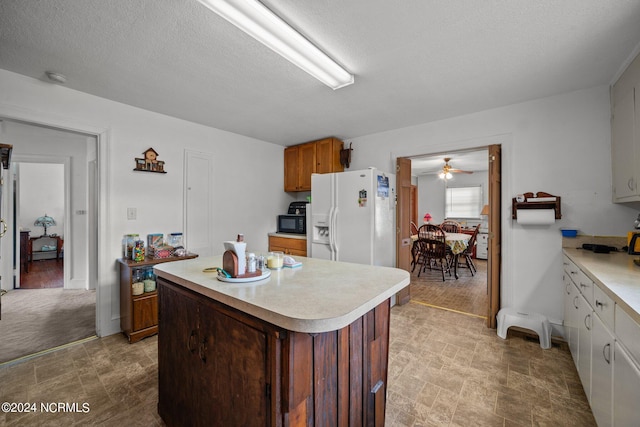 kitchen with white refrigerator with ice dispenser, a textured ceiling, a center island, ceiling fan, and white cabinets