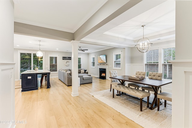 dining room with decorative columns, light hardwood / wood-style flooring, ornamental molding, ceiling fan with notable chandelier, and sink