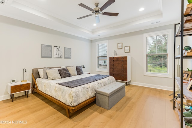 bedroom with ornamental molding, a tray ceiling, light wood-type flooring, and ceiling fan