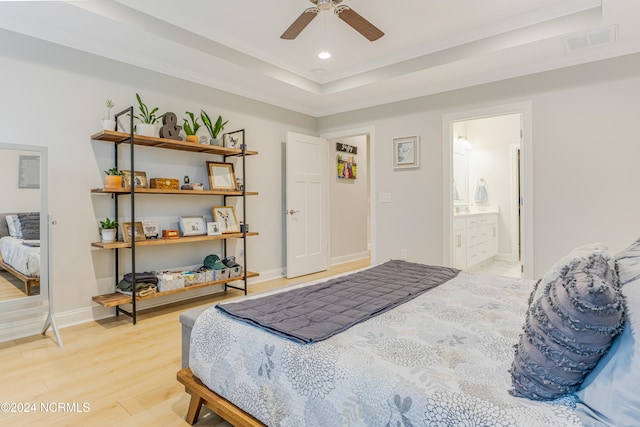 bedroom with ensuite bath, hardwood / wood-style flooring, a raised ceiling, and ceiling fan