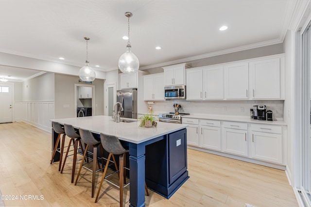 kitchen featuring white cabinets, stainless steel appliances, hanging light fixtures, and an island with sink