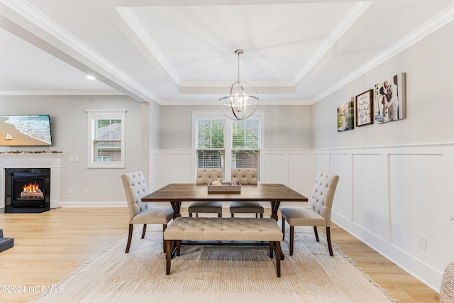 dining space with ornamental molding, a chandelier, light wood-type flooring, and a raised ceiling