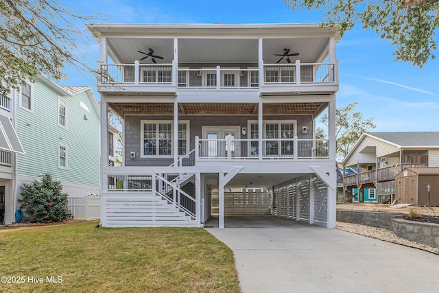 raised beach house with covered porch, stairway, a ceiling fan, a carport, and driveway