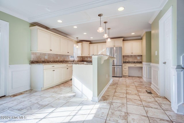 kitchen with light stone countertops, backsplash, ornamental molding, pendant lighting, and stainless steel refrigerator