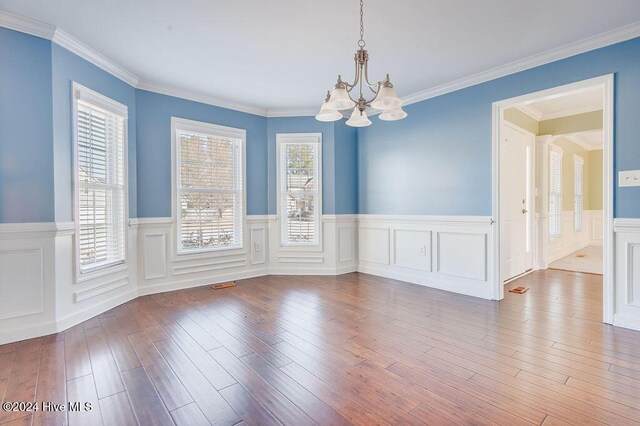 unfurnished room with a healthy amount of sunlight, wood-type flooring, a chandelier, and ornamental molding