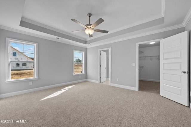 unfurnished bedroom featuring a closet, a raised ceiling, light carpet, a walk in closet, and ornamental molding